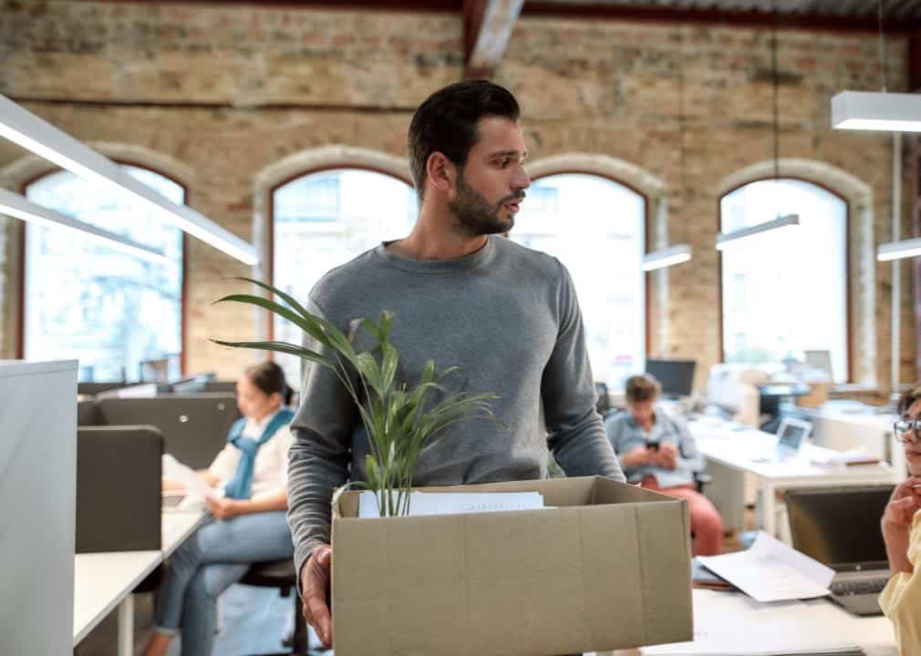 A man is leaving his job with a box holding all of the stuff from his desk.