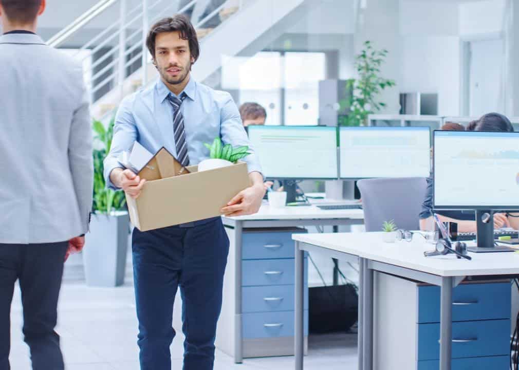 An employee is leaving his office for the final time, while holding a box of all of his stuff.